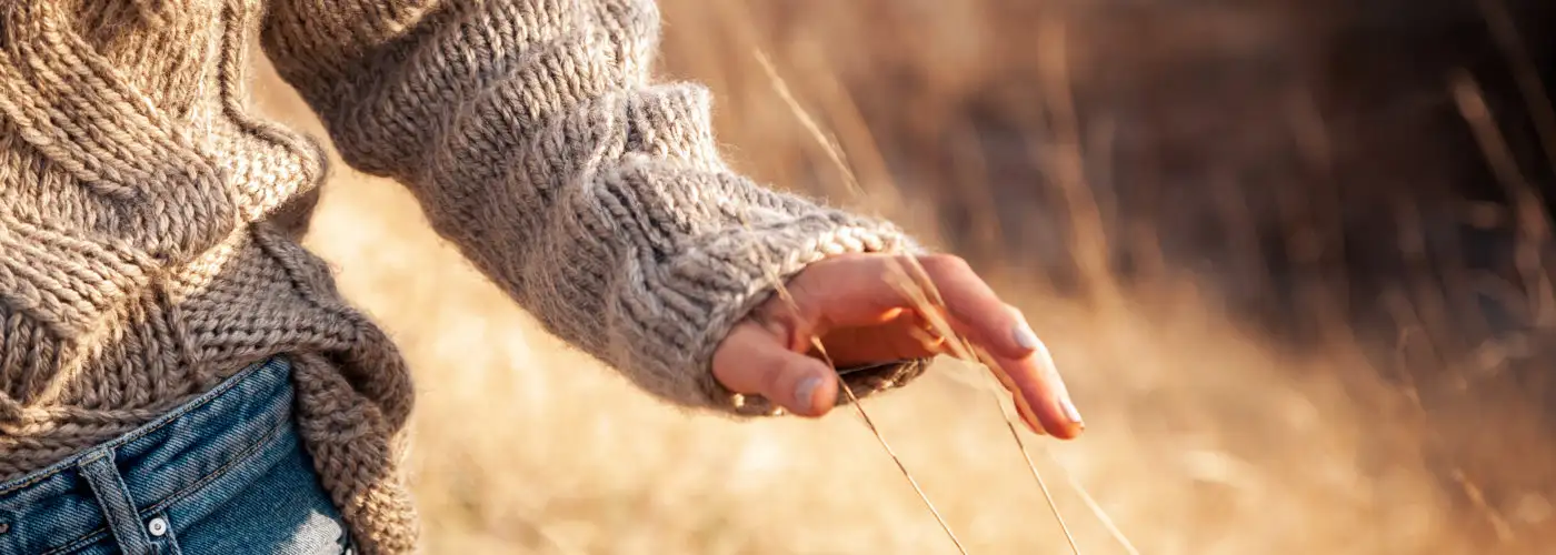Close up of person's hand brushing through tall fall grass, the person is wearing a knit sweater