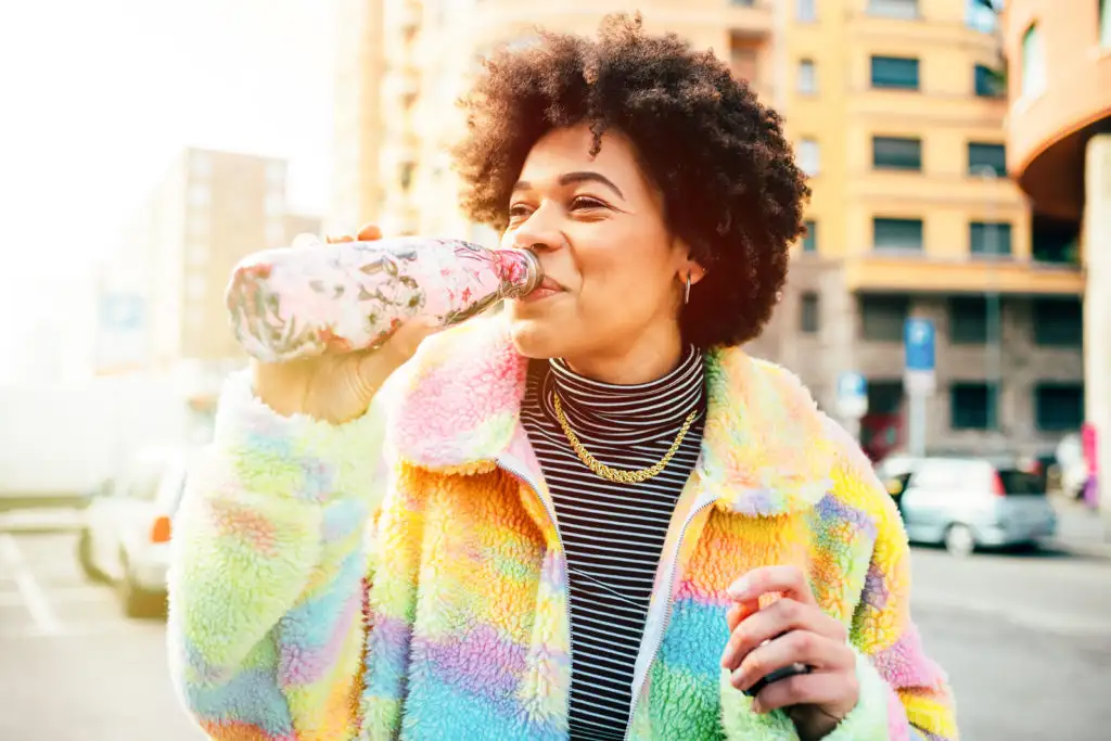 Woman in colorful coat drinking from a reusable water bottle