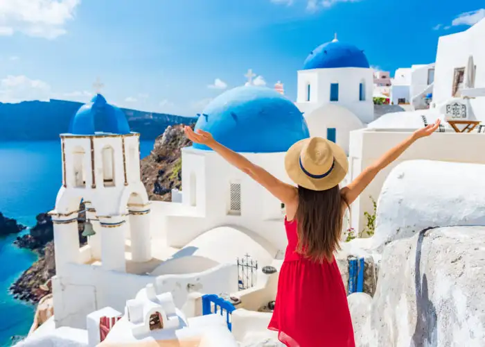 Woman with her hands in the air overlooking a landscape of white and blue houses on Santorini in Greece