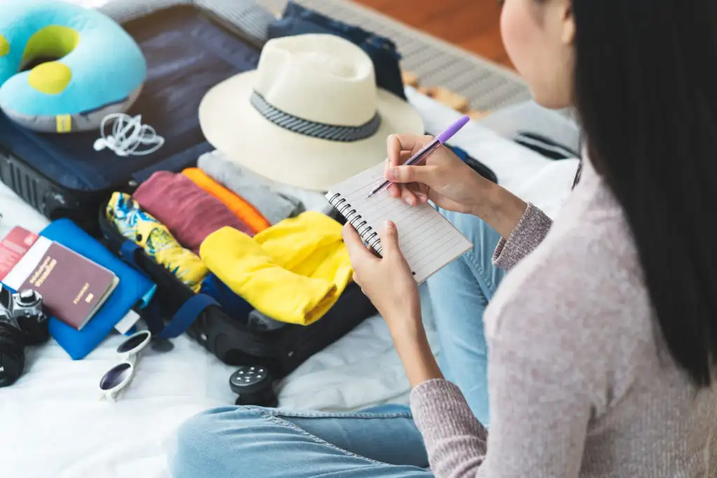 Woman writing a list while looking at her partially packed suitcase
