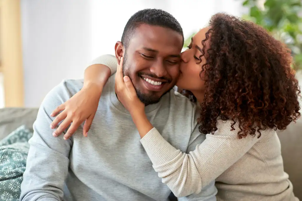 Woman kissing man's cheek while sitting on couch