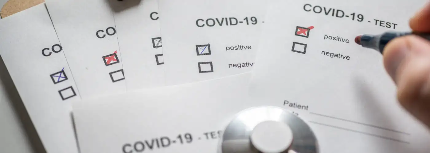 Close up of doctor filling out a stack of paperwork showing several positive COVID test results