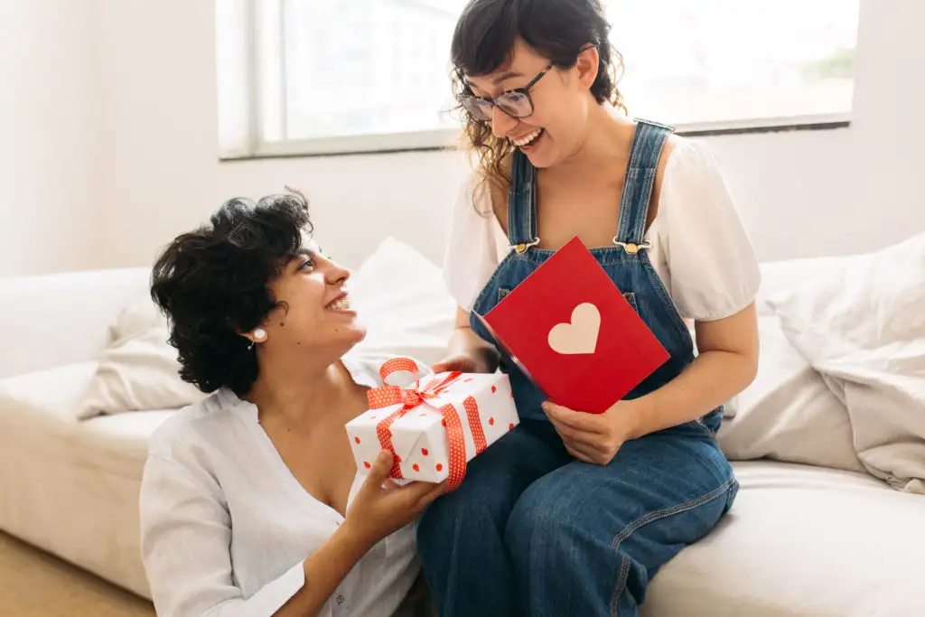 Couple exchanging Valentine's day gifts, one sitting on the couch and one sitting on the floor
