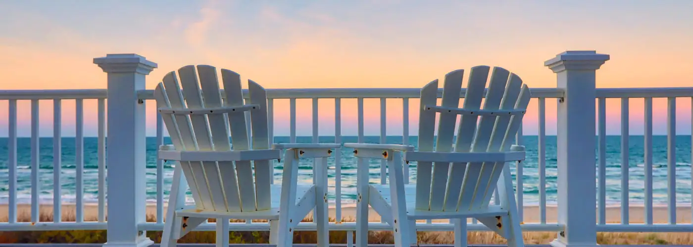 Adirondack chairs on a deck overlooking the ocean at sunset