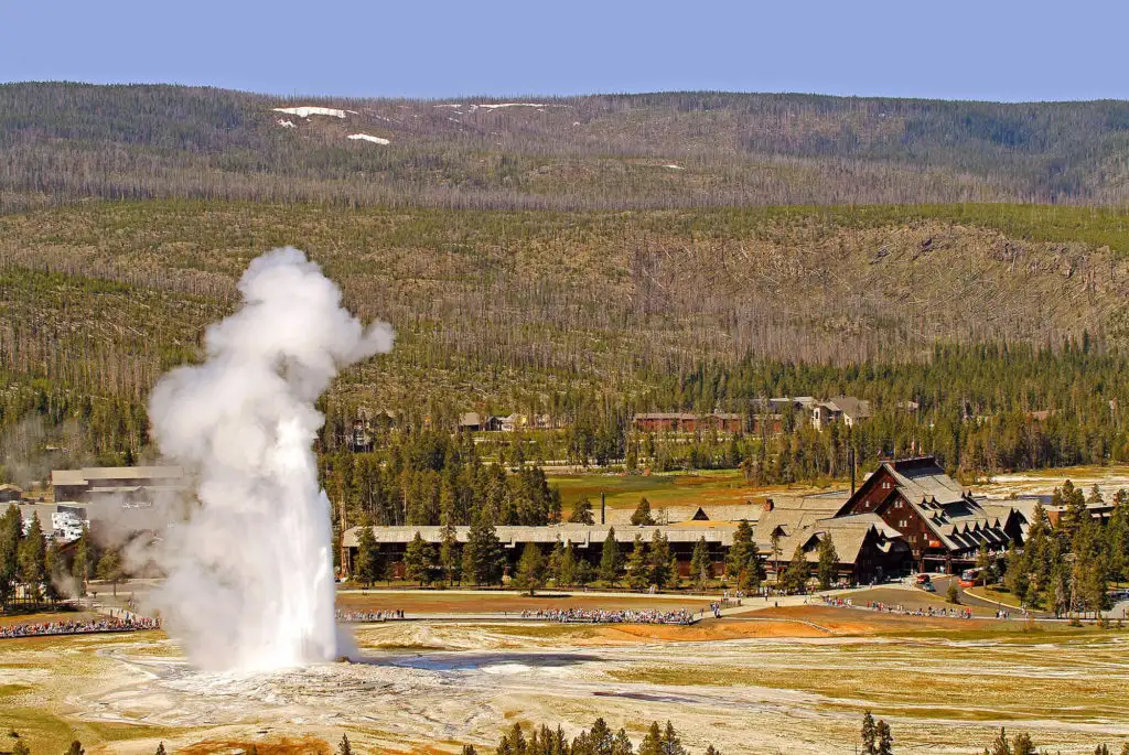 Distant view of Old Faithful Inn and erupting Old Faithful Geyser 