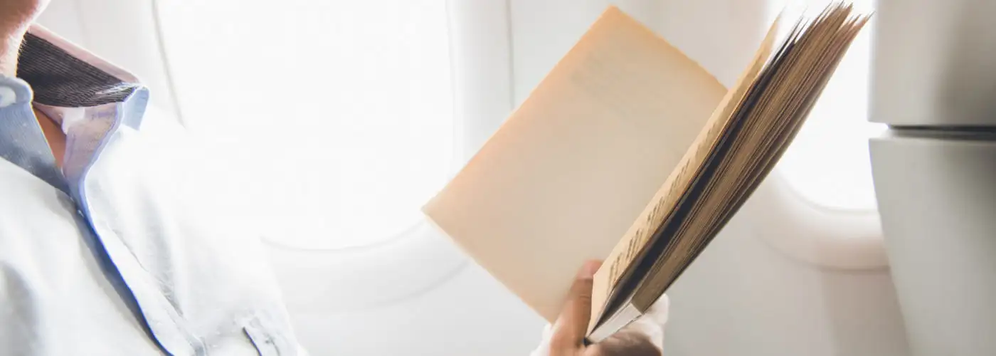 Close up of person holding and reading from a paperback book on a plane