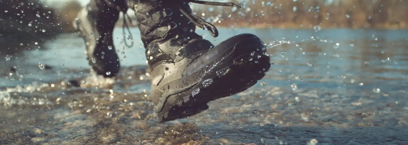 Close up of someone wearing fuzzy waterproof boots, splashing through a puddle on a cobblestone surface