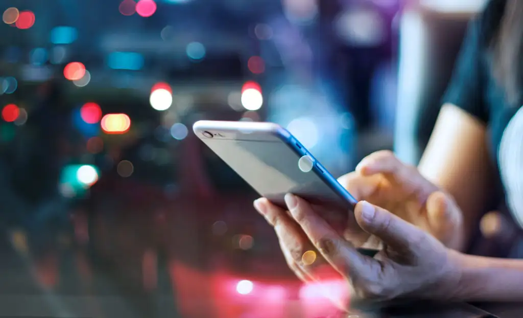 Close up of person using a smartphone with a line of traffic unfocused in the background