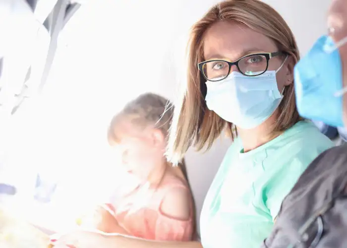Two adults and a child sitting in a row on a plane, the adults are wearing medical face masks