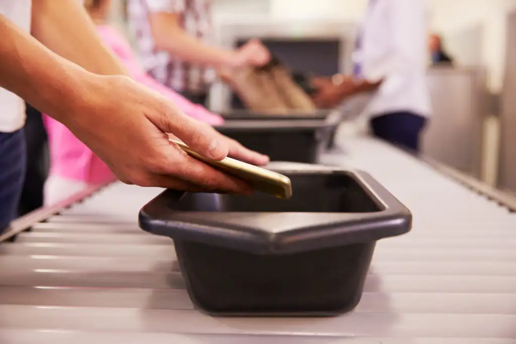 Close up of person putting their smartphone in a security bin going through airport security