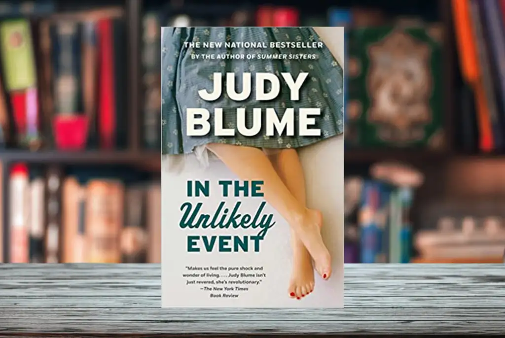 Cover of Judy Blume's book In The Unlikely Event superimposed on a bookshelf with shelves of books in the background
