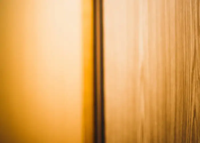 Warm toned image of a hotel room door with peephole in an orange hallway