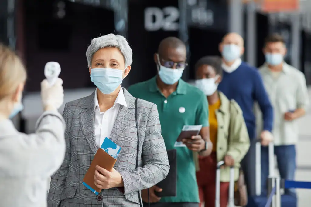 Group of masked people waiting in line at the airport to have their temperature taken