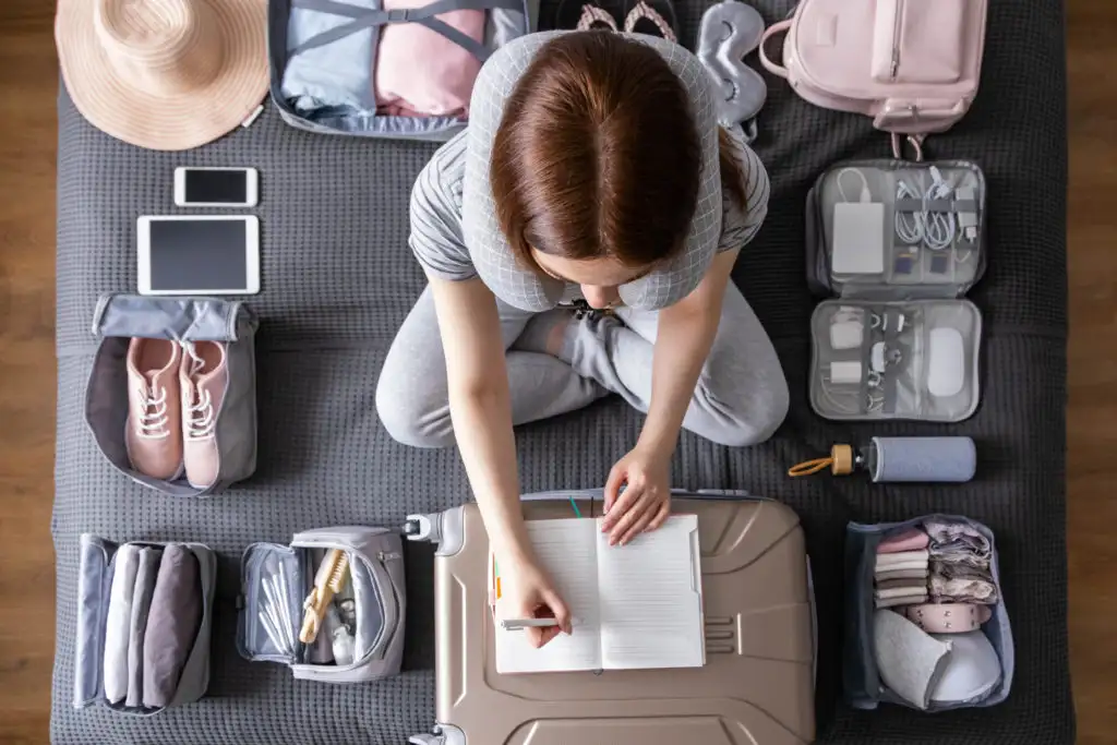 Bird's eye view of a woman surrounded by packing items, writing a packing list on her suitcase