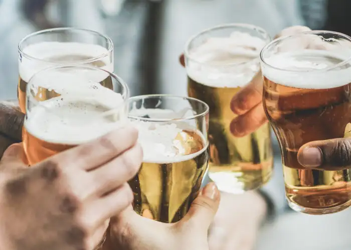 Close up of hands clinking beer glasses in a large group
