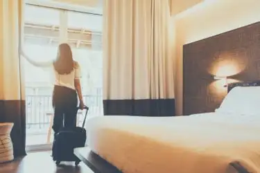 Woman pulling a rolling suitcase, looking out the window of her hotel room