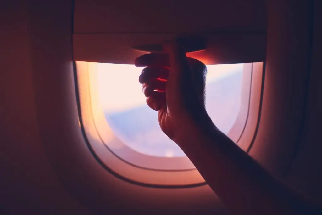 Close up of hand pulling down shade on window in airplane