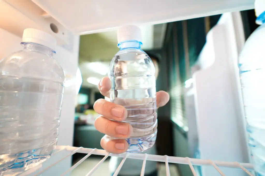 Hand taking water bottle out of fridge
