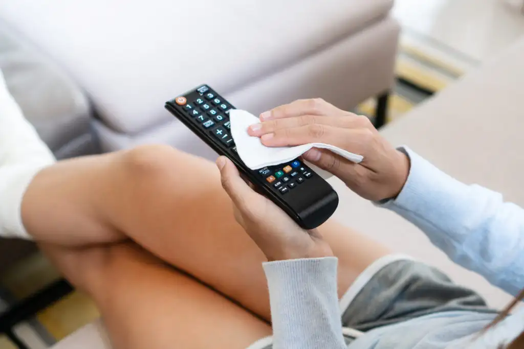 Close up of woman disinfecting a tv remote with a sanitizing wipe