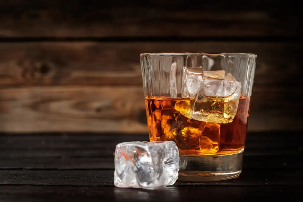 Glass of whiskey and ice on a dark wooden table and backdrop