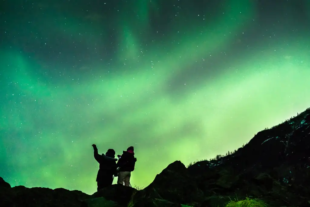 Silhouette of two people against the northern lights in the sky