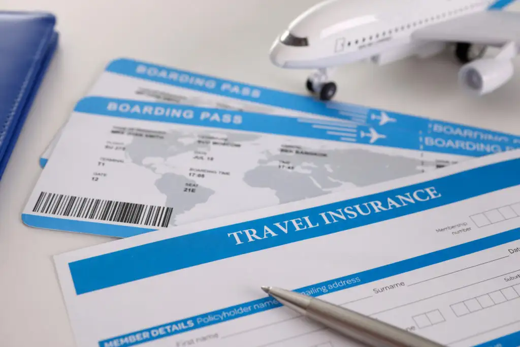 Two boarding passes, a model plane, a travel insurance document, and a pen on a white table