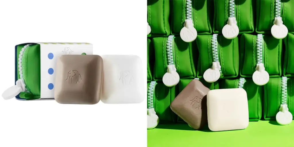 Close up of Drunk Elephant Baby Bar Travel Duo With Case (left) and two Drunk Elephant cleansing bars resting against a large pile of green travel cases (right)