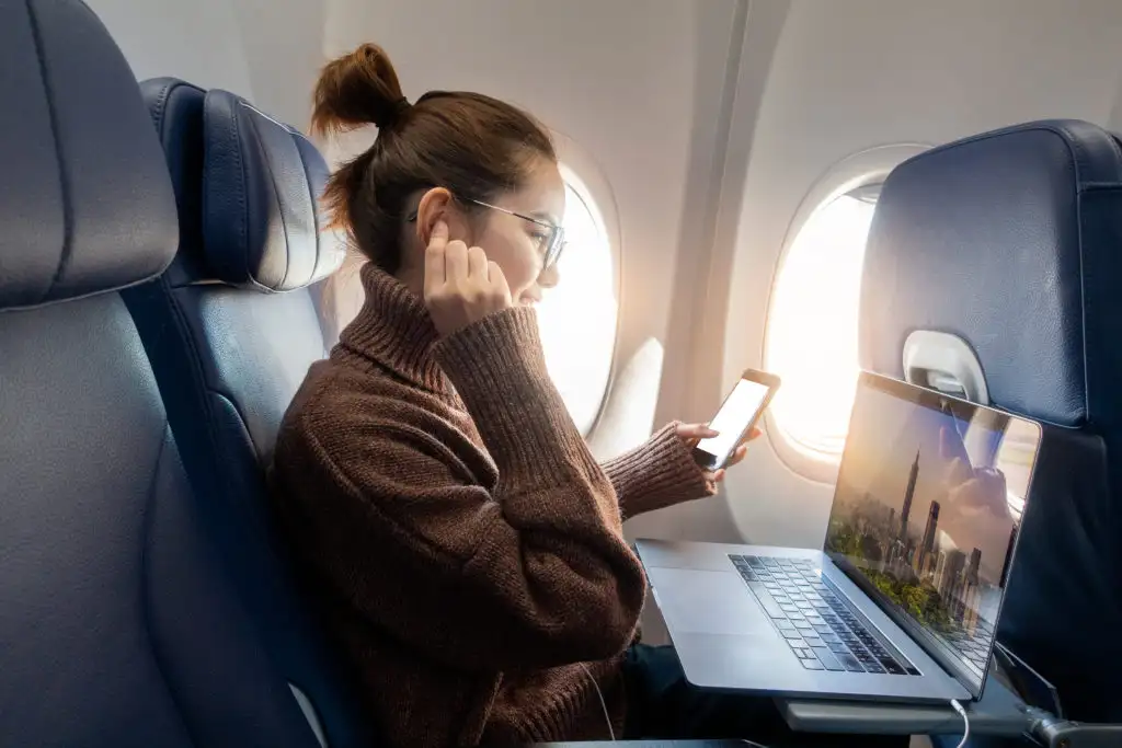 Close up of woman wearing cozy sweater and listing to music while using her laptop on an airplane