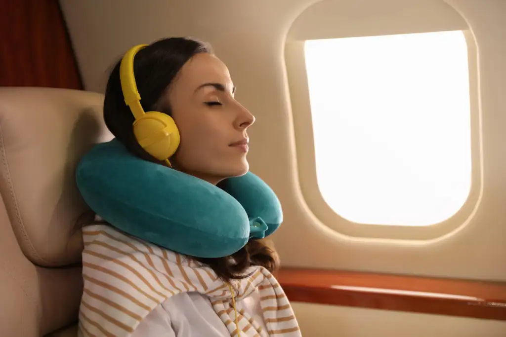Woman wearing a blue travel neck pillow and yellow headphones sleeping on a plane
