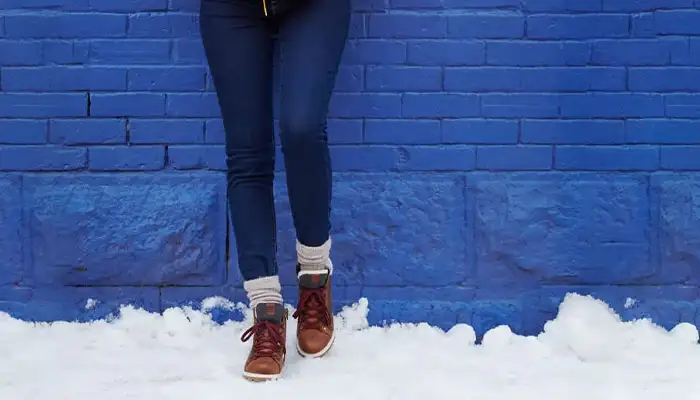Close up of person leaning against a blue brick wall in the snow wearing Kamik Rouge Hike 3 boots