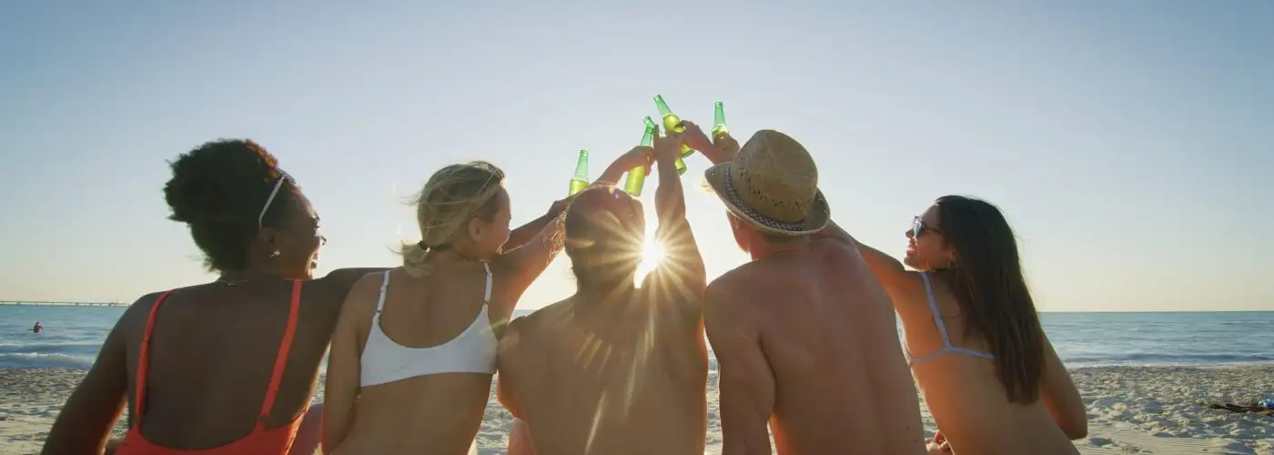 Group of friends clinking beer bottle together on beach