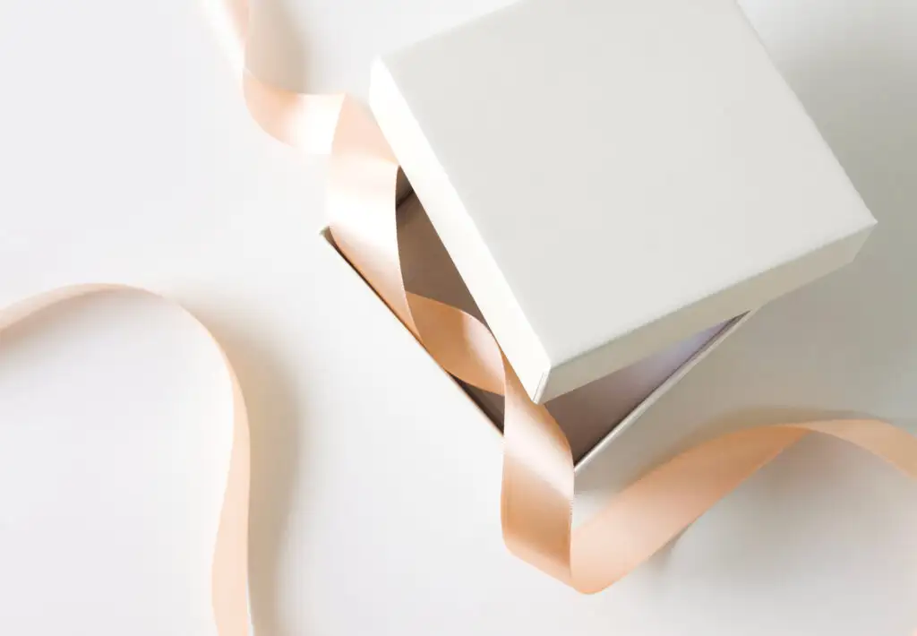 Slightly open white gift box on a white table with a light pink ribbon