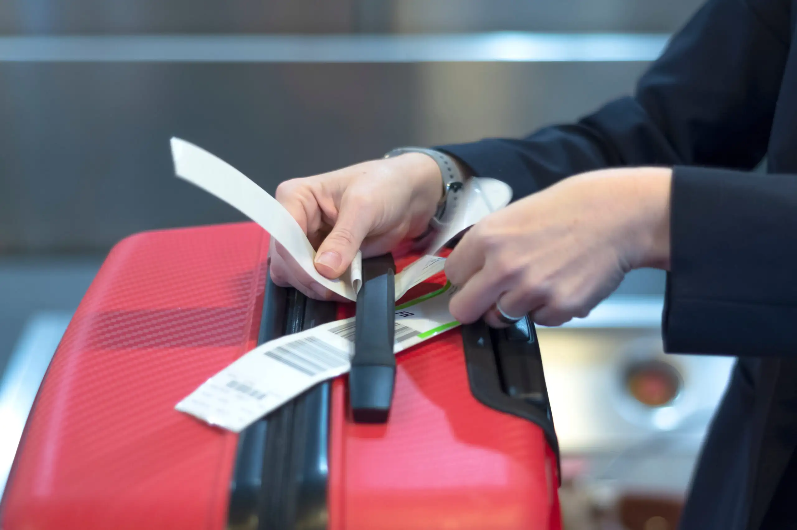 Close up of person adding a luggage tag to their red suitcase in an airport