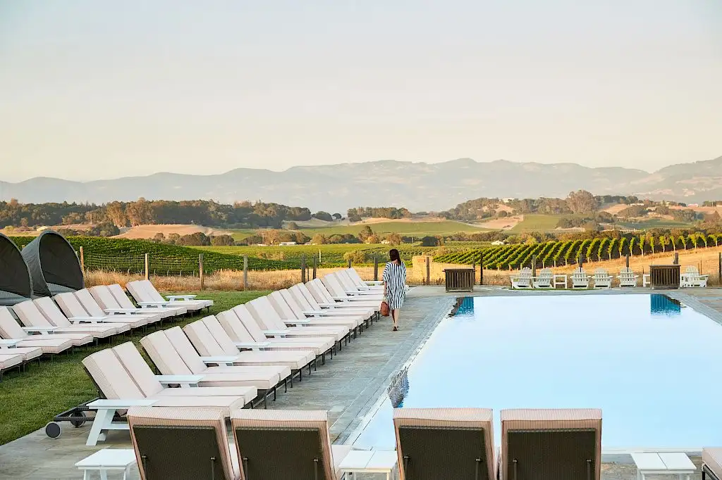 Woman walking next to a pool surrounded by lounge chairs overlooking rolling hills at Carneros Resort and Spa