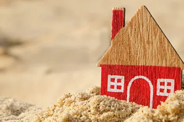Small wooden model of a house in the sand