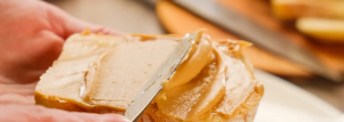 Close up of person spreading peanut butter on slice of bread