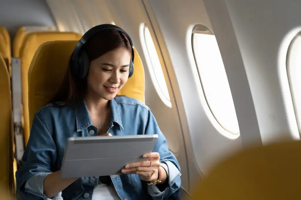 Person scrolling through iPad with noise cancelling headphones on while seated in an airplane cabin