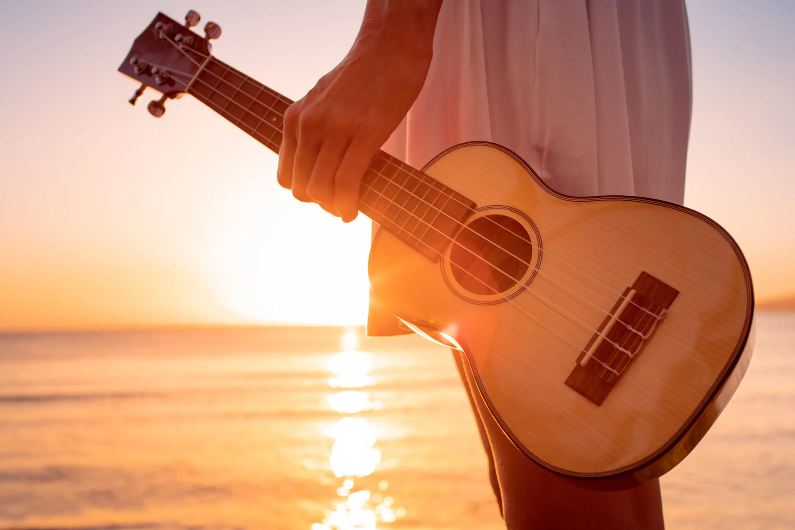 Close up of person holding a ukulele by the ocean at sunset