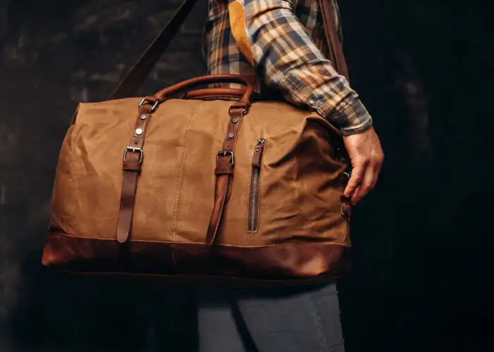 Close up of man holding a brown leather duffel bag