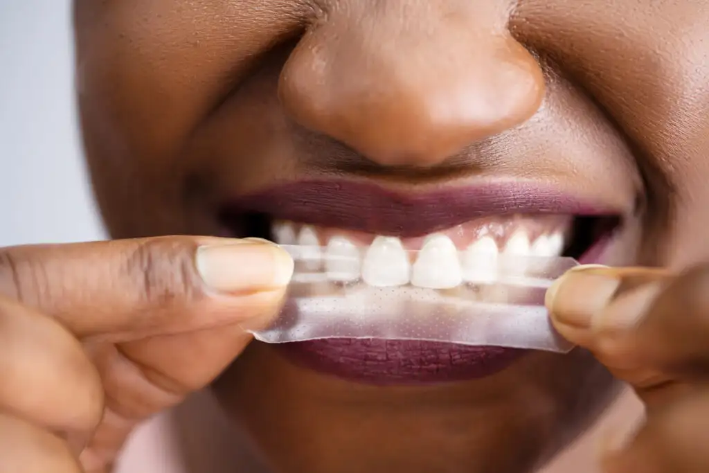 Close up of person applying a teeth whitening strip to their top teeth