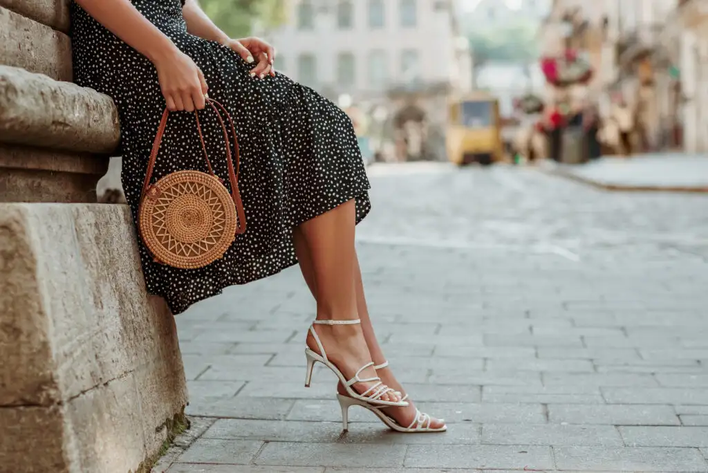 Close up of person wearing dress and low heels resting on a stone wall in a European city