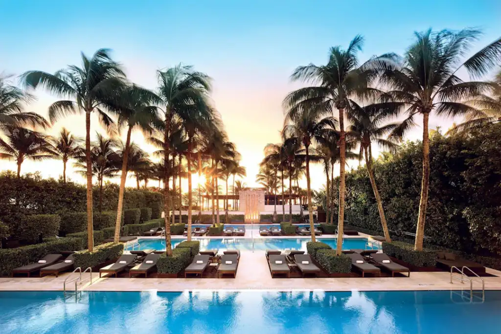 Looking over The Setai's pools withpalm trees blowing in the wind and the sunset in the background