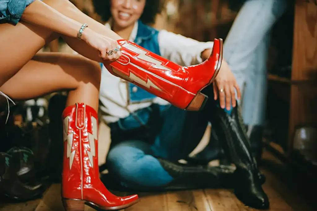 Woman trying on red cowboy boots with woman in the background watching