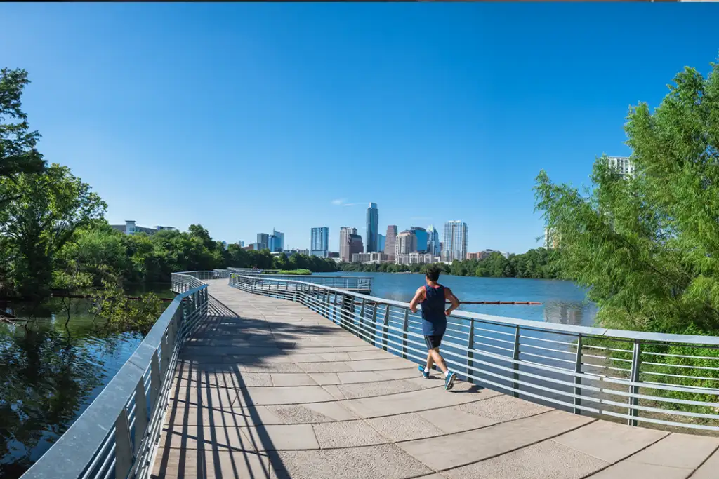 Panorama view Downtown Austin, Texas, US along Colorado River at daytime with cloud blue sky. View from Ann and Roy Butler Hike-and-Bike Trail and boardwalk at Lady Bird Lake, unidentified man running