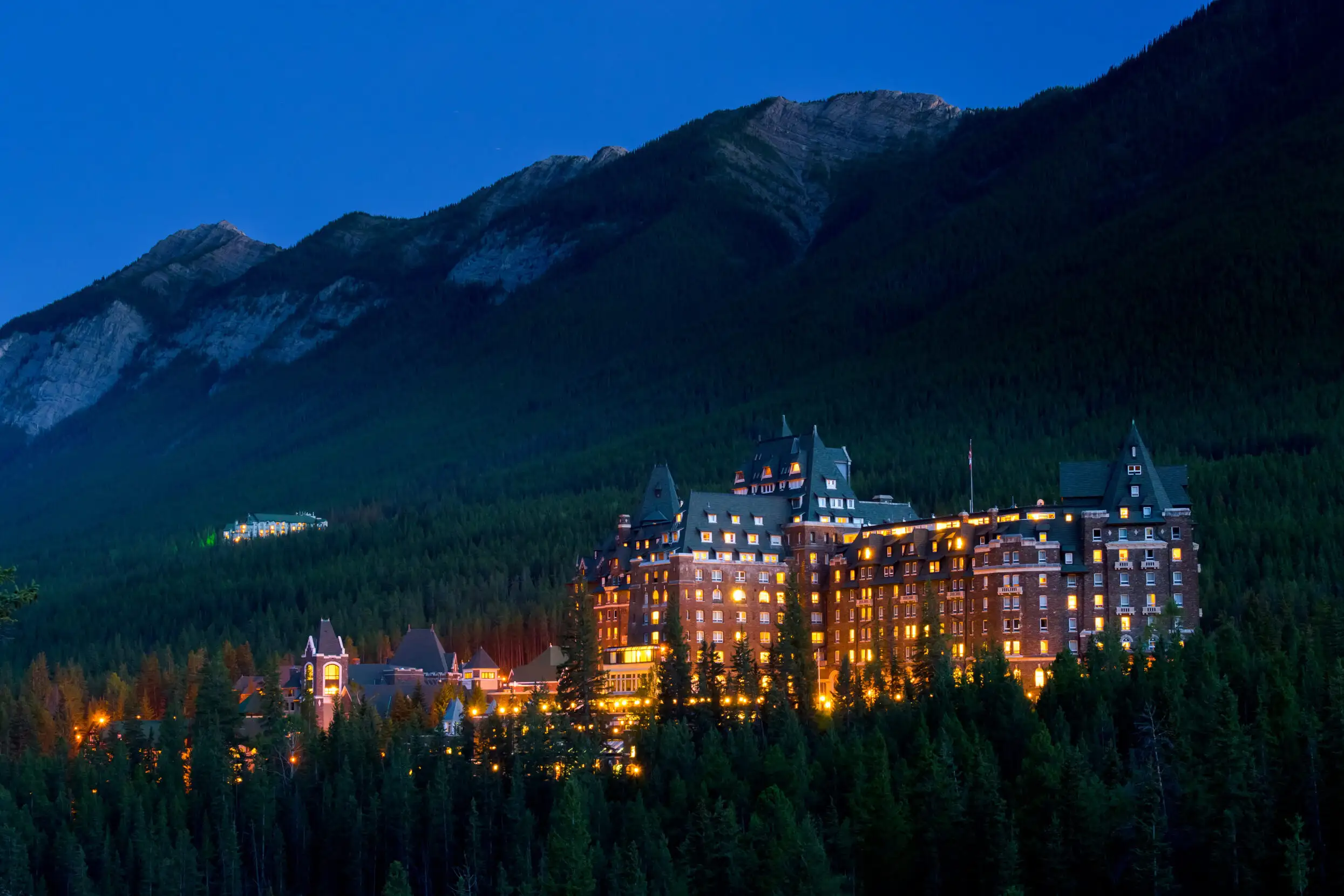 Fairmont Banff Springs castle in the wilderness at a distance, illuminated at by window lights at night