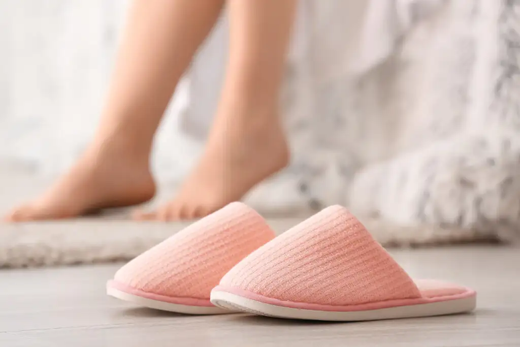 Pink slippers on the floor with feet out of focus in the background
