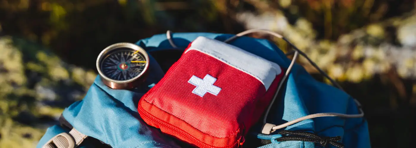Compass and first aid kit on a backpack in the woods