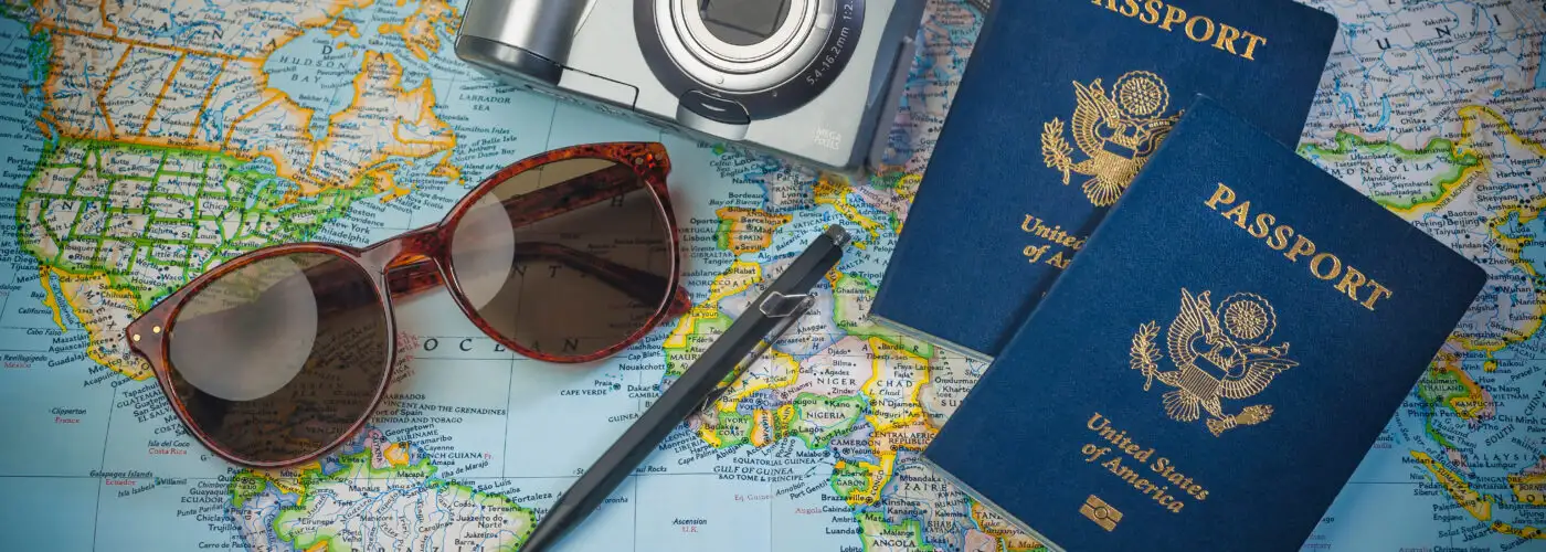 Passports, a camera, sunglasses, and a pen resting on top of a world map