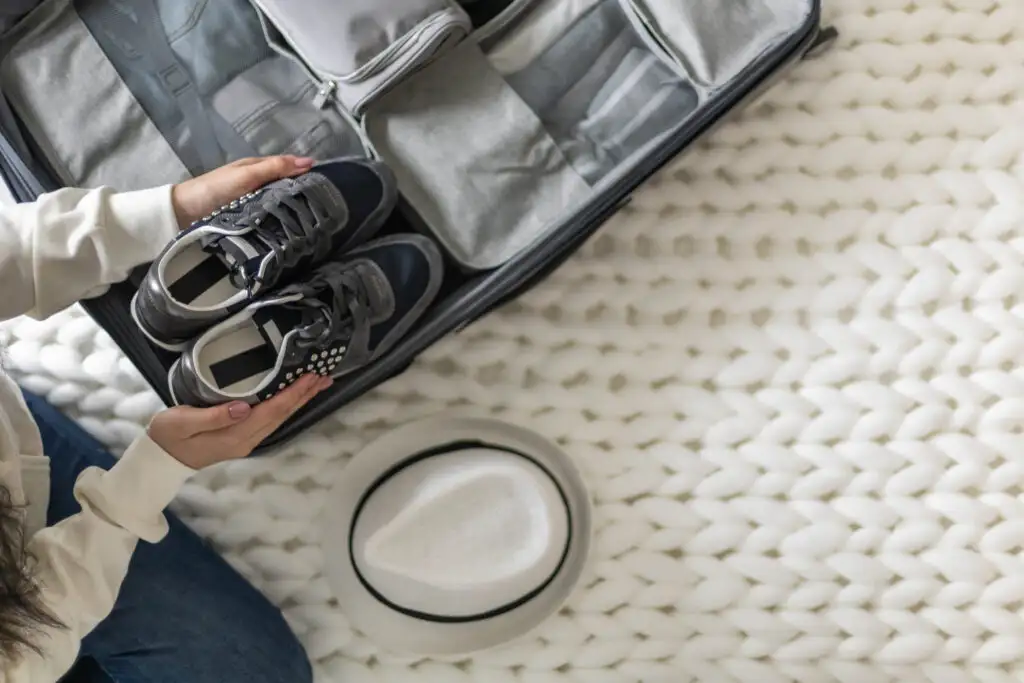 Overhead view of someone packing a pair of sneakers in a suitcase