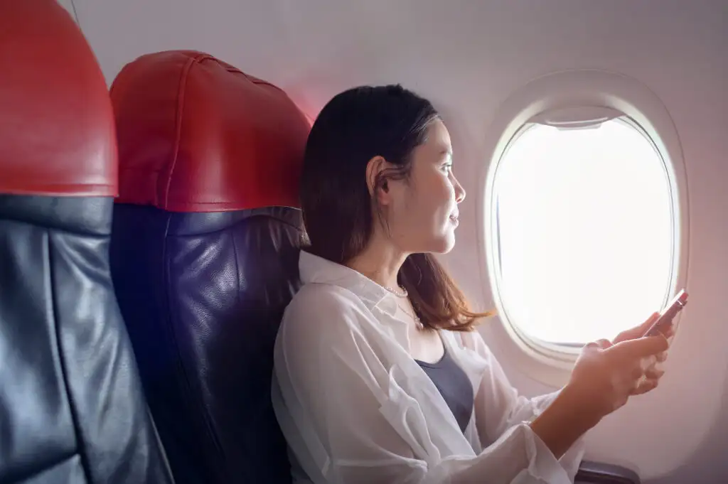 Woman using phone, looking out airplane window